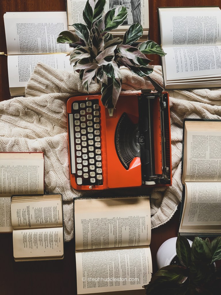 Orange typewriter surrounded by books.